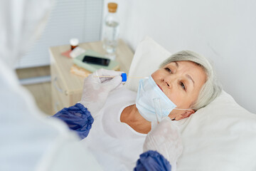 Naklejka premium Unrecognizable doctor wearing protective suit taking senior woman's nasal swab for Covid-19 test using stick