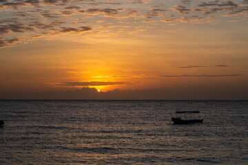 Orange sunset over the Indian Ocean on the coast of Pemba Island, Tanzania, with low clouds on the horizon and silhouette of a fishing boat.