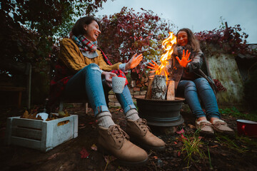 three friends relax comfortably and drink wine on an autumn evening in the open air by the fire in the backyard.