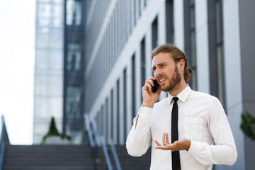 Portrait of a successful young businessman. A curly-haired man in a white shirt with a telephone against the background of a modern business center.