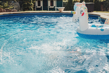 Water drops splash in blue water in swimming pool. Inflatable swimming large toy unicorn floating in water. Outdoors summer seasonal fun activity in water. Leisure time at home backyard pool. © anoushkatoronto