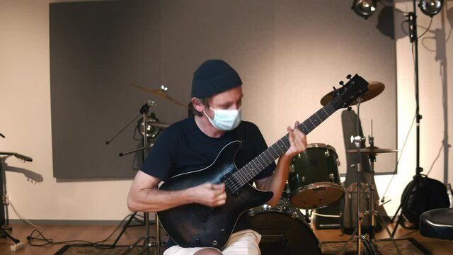 Professional audio studio. Man playing guitar. Life of musicians across the coronavirus. The caucasian male person wearing the health mask throughout the COVID-19 times. 