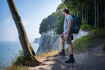 hiker with backpack looking down a chalk cliff coast