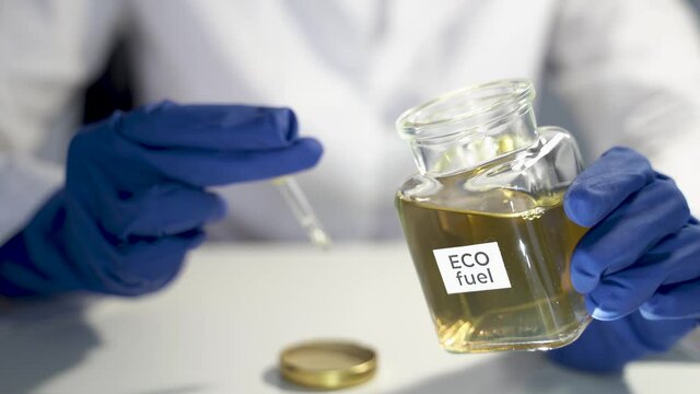 Scientist girl using a pipette takes eco-fuel from a glass flask for testing