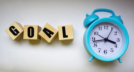 Word goal made with wooden blocks of letters next to blue alarm clock on white background