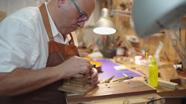 Luthier with violin bridge in workshop