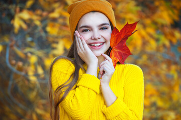 Beautiful girl walking outdoors in autumn. Smiling girl collects yellow leaves in autumn.