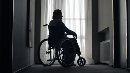 Old woman sit on wheelchair in a front of the window - Powered by Adobe