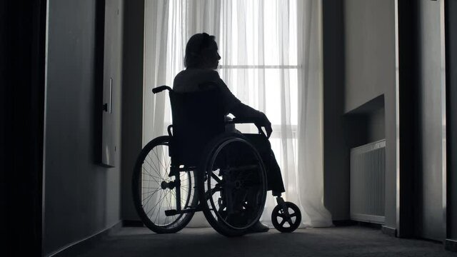 Old woman sit on wheelchair in a front of the window