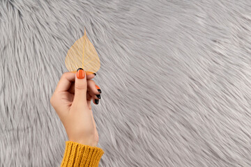 Manicured woman's hand holding yellow leaf on gray fluffy background