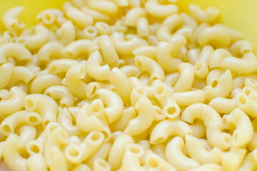 boiled pasta horns without anything close up, yellow background
