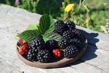 Ripe blackberries in a clay plate on a wooden background.