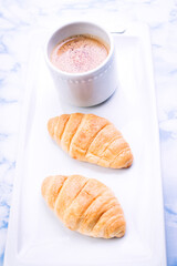 Breakfast consisting of croissants and coffee with milk with white dishes.