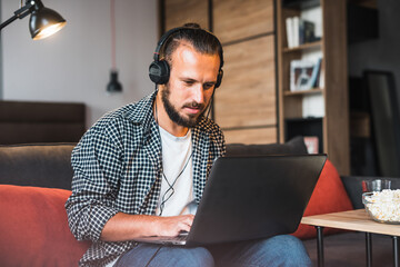 Man relaxing on sofa using laptop and smartphone.	Man sitting on the sofa of a living room and working on his laptop.