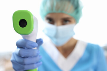Woman doctor in protective mask and gloves holds thermometer in her hands to measure body temperature. Non-contact thermometry for coronavirus concept