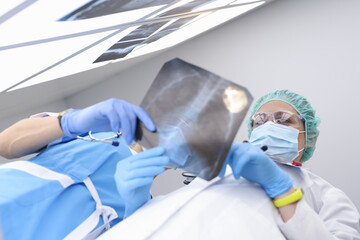 Two doctors wearing protective medical masks and gloves are holding an X-ray. Coronavirus...