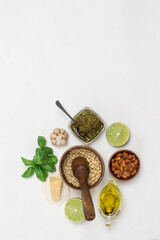 Pesto sauce and ingredients. Pine nuts in wooden mortar, unpeeled pine nuts in bowl, olive oil, pesto bowl, basil leaves, parmesan, garlic, lemon.