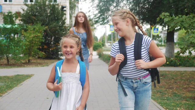 group of schoolchildren walking to school along the path. happy family school concept.little schoolgirl with backpack and textbook. schoolgirls walk along in the park education school to for lessons