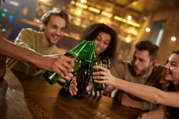 A group of friends in the bar watching sports match on TV together, drinking beer, clinking bottles and cheering for team