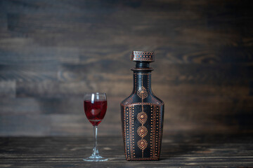 Homemade tincture of red cherry in a decorative bottles and a wineglass on wooden background,...