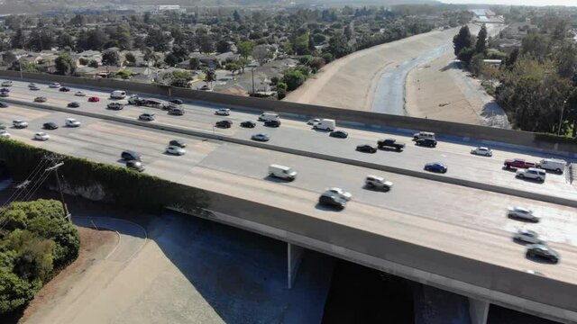Aerial view of traffic on 405 freeway over LA river on a sunny day, in Los Angeles, California camera slow pan up and to the left revealing highway and neighborhood