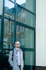 Fototapeta premium Handsome businessman freelancer in grey coat and biege trousers smiles and walking down the sidewalk