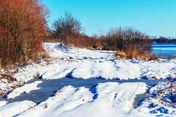 Snow-covered shore river with a puddle in sunny weather