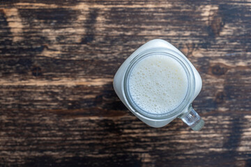 Glass jar of banana milkshake on wooden background. Top view, copy space