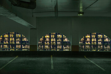 View at night through the arches of an empty concrete  parking garage with apartment lights in background orange and teal toning nobody
