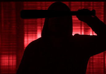 unrecognizable man in a jacket with a hood holds a baseball bat. Dangerous man with baseball bat...