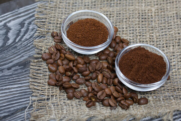 Coffee beans on coarse linen. Ground coffee in containers. On a surface of brushed pine boards painted black and white.