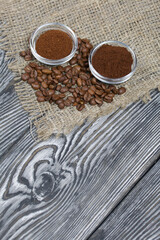 Coffee beans on coarse linen. Ground coffee in containers. On a surface of brushed pine boards painted black and white.
