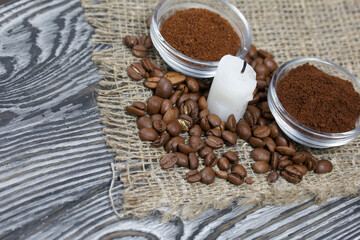 Coffee beans on rough linen and candle stub. Ground coffee in containers. On a surface of brushed pine boards painted black and white.