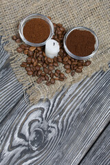 Coffee beans on rough linen and candle stub. Ground coffee in containers. On a surface of brushed pine boards painted black and white.