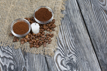 Coffee beans on rough linen and candle stub. Ground coffee in containers. On a surface of brushed pine boards painted black and white.