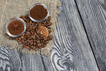 Coffee beans on coarse linen. Ground coffee in containers and spices. On a surface of brushed pine...