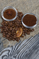 Coffee beans on coarse linen. Ground coffee in containers and spices. On a surface of brushed pine boards painted black and white.