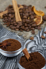 Coffee beans on coarse linen. Ground coffee in containers and spices. On a surface of brushed pine boards painted black and white.