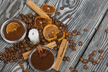 Coffee beans on rough linen and candle stub. Ground coffee in containers and spices. On a surface of brushed pine boards painted black and white.