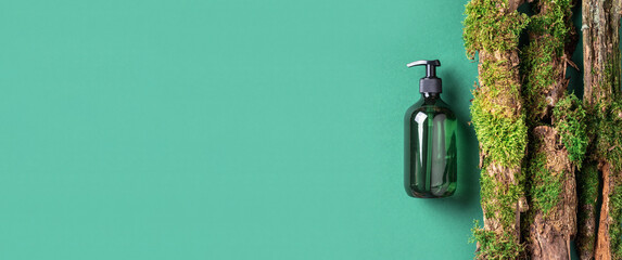 Green glass bottle of shampoo, soap, conditioner on green background with natural moss over bark, wood. Top view, copy space. Blank label for mock-up. Skin care, organic body treatment, spa concept