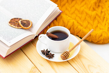 aromatic hot cinnamon tea covered with a warm scarf on a wooden autumn background. honey dipper with honey. comfortable reading a book