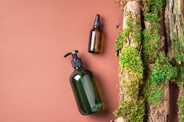 Unlabelled cosmetic bottle on brown background, natural moss over branches, bark. Skin care,...