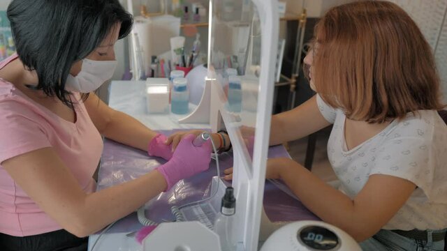 limpieza con torno de esteticista en cl&iacute;nica de belleza para ma&ntilde;os u a&ntilde;as detr&aacute;s de una mampara y mascarilla