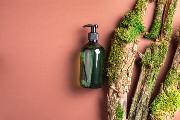 Green glass bottle of shampoo, soap, conditioner on brown background with natural moss over bark, wood. Top view, copy space. Blank label for mock-up. Skin care, organic body treatment, spa concept