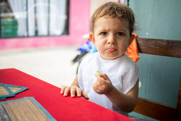 cute little toddler kid in bib frowns dissatisfied with tried food sitting at a table on a street cafe terrace