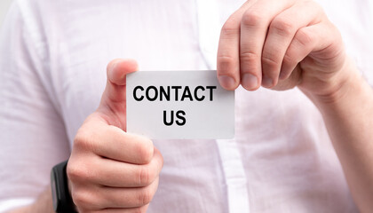 Businessman in white shirt hold a card with text Contact us in his hands - business concept