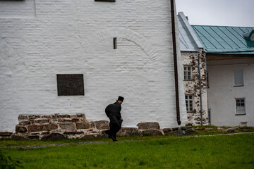 a monk in black clothes walks in the rain through the territory of the fortress-monastery on the Solovetsky Islands