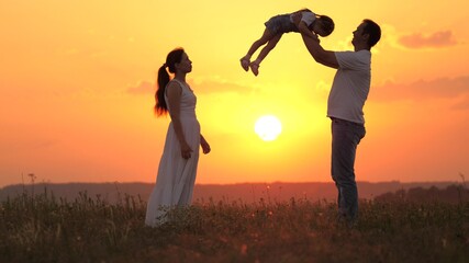 dad plays with his little daughter, happy to throw child into air, happy mom admires her family. mommy daddy and baby, family is resting at sunset in field. happy healthy family walking in fresh air.