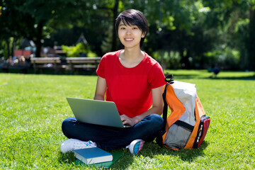 Laughing east asian male student learning at computer at campus of university