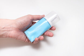 A hand holding blue plastic conteiner, bottle of moisturising cream, lotion with dosator and cap on white background